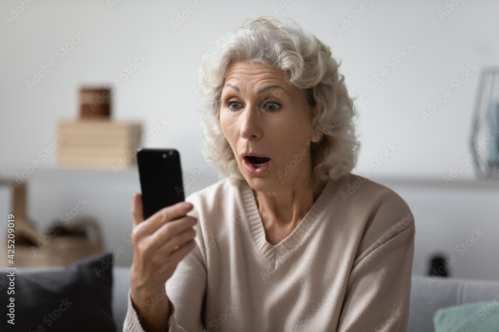Shocked elderly lady staring at smartphone with open mouth. Excited senior 60s woman reading surprising message on phone, talking via video call, getting amazing news, having problems with cell Shocked elderly lady staring at smartphone with open mouth. Excited senior 60s woman reading surprising message on phone, talking via video call, getting amazing news, having problems with cell