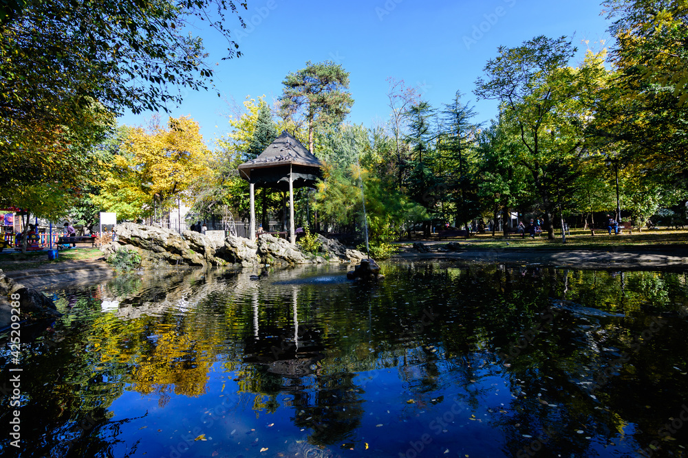 Landscape with the small lake and green and yellow trees in Ion Voicu Park, also known as Ioanid Park, in Bucharest, Romania, in a sunny autumn day. Landscape with the small lake and green and yellow trees in Ion Voicu Park, also known as Ioanid Park, in Bucharest, Romania, in a sunny autumn day.