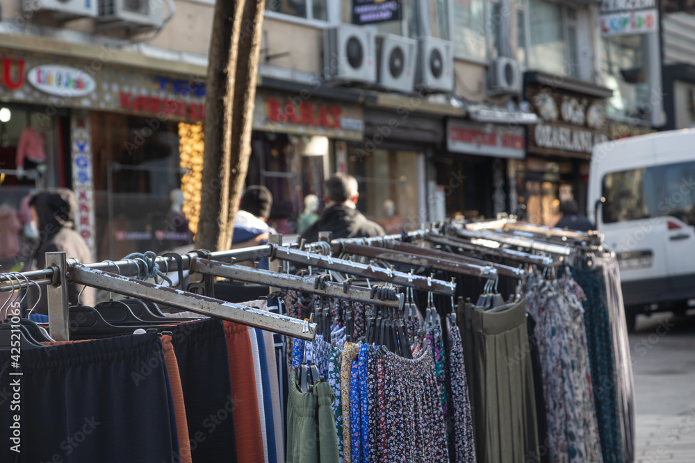 Naklejka premium A clothing rack stands outdoors for street trading. In focus, women's dresses and pants hang on the counter against the backdrop of the busy streets of Istanbul