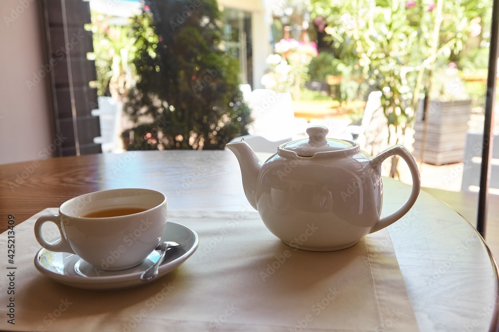 The table is set for tea. A teapot and a tea cup are placed on the table overlooking the terrace The table is set for tea. A teapot and a tea cup are placed on the table overlooking the terrace