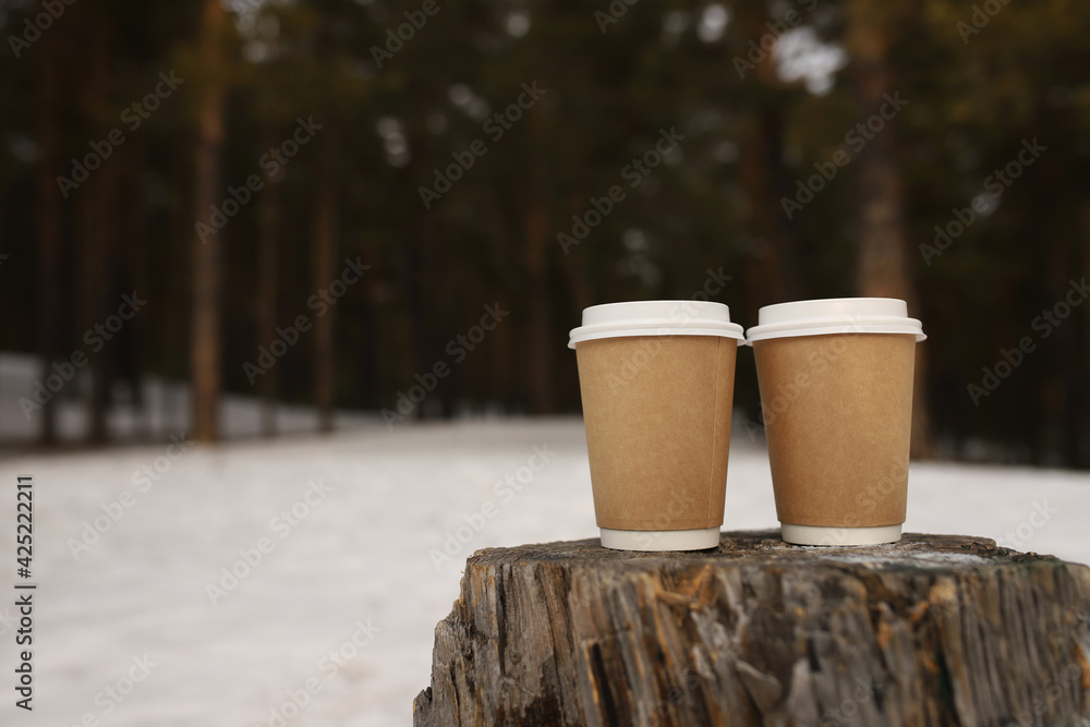 Two disposable glasses stand on a stump in a snow-covered forest. A place for text. Two disposable glasses stand on a stump in a snow-covered forest. A place for text.