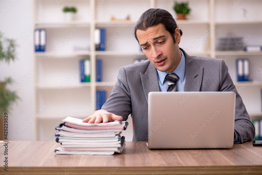 Young male employee unhappy with excessive work in the office Young male employee unhappy with excessive work in the office