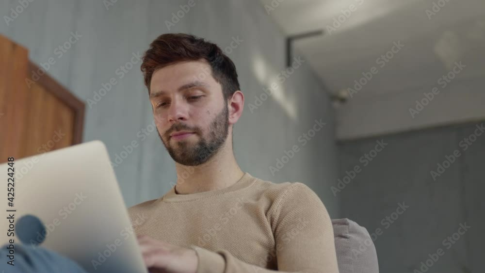 Young guy working on a laptop on the couch. Man typing with laptop on couch Young guy working on a laptop on the couch. Man typing with laptop on couch