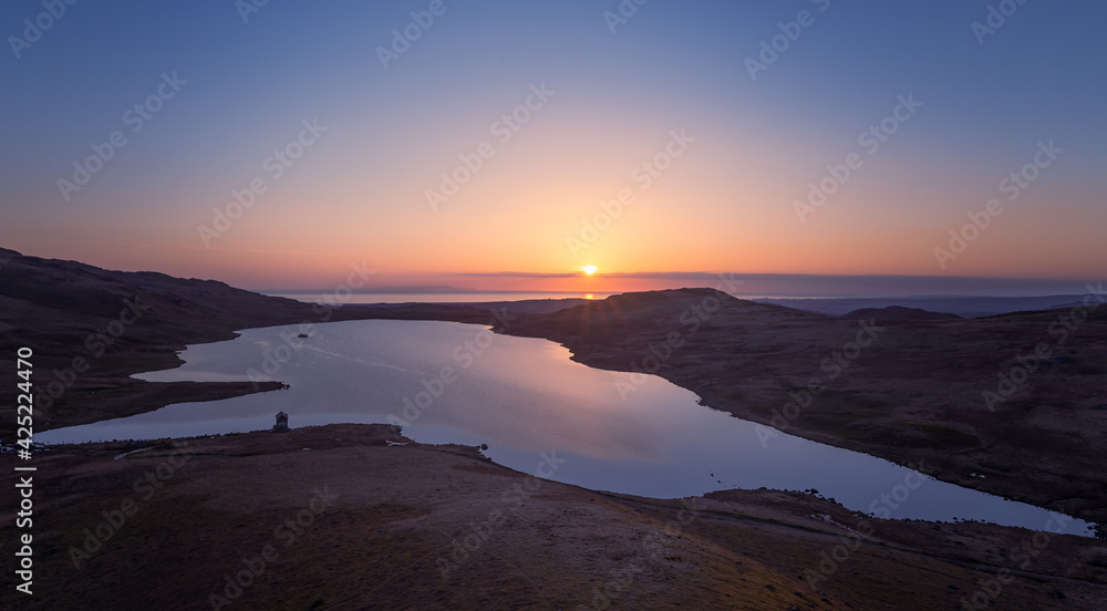 Sunset over a calm lake with an island on the horizon far out to sea under an electric blue sky Sunset over a calm lake with an island on the horizon far out to sea under an electric blue sky