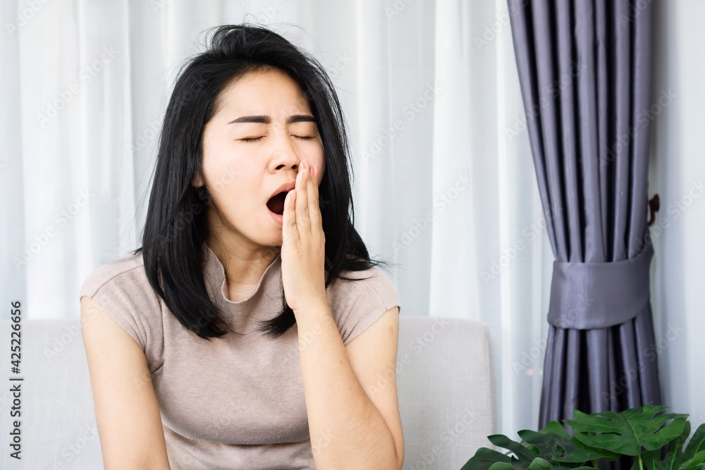 sleepless Asian woman yawning and tired from insomnia sitting on sofa hand covering her mouth feeling sleepy sleepless Asian woman yawning and tired from insomnia sitting on sofa hand covering her mouth feeling sleepy