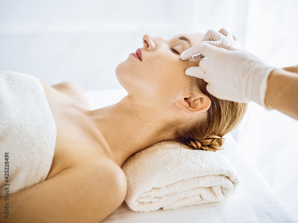 Beautiful woman receiving beauty injections with closed eyes in medical center. Beautician doctor hands doing beauty procedure to female face with syringe. Cosmetic medicine and surgery concept