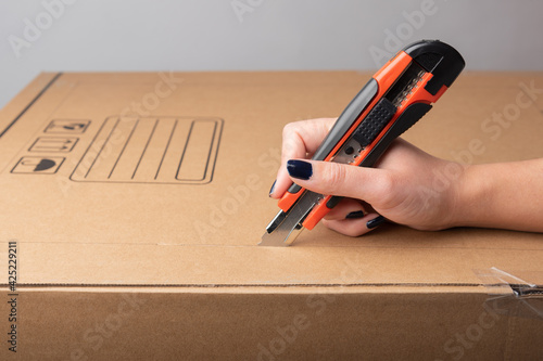 Female hand cutting with utility knife carton box