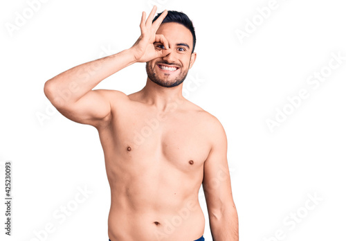 Young handsome man wearing swimwear smiling happy doing ok sign with hand on eye looking through fingers