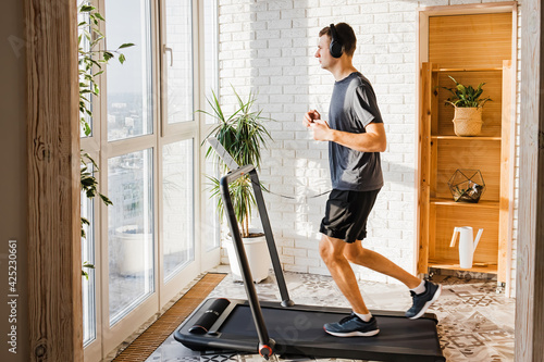 Foto Young man jogging on the modern compact treadmill at his home