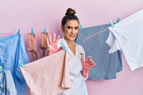Beautiful brunette young woman washing clothes at clothesline disgusted expression, displeased and fearful doing disgust face because aversion reaction. with hands raised