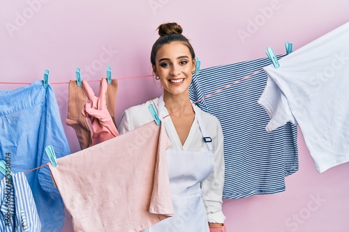 Beautiful brunette young woman washing clothes at clothesline showing and pointing up with fingers number two while smiling confident and happy.
