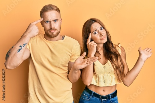 Young couple of girlfriend and boyfriend hugging and standing together confused and annoyed with open palm showing copy space and pointing finger to forehead. think about it.