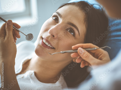 Smiling brunette woman being examined by dentist at dental clinic. Hands of a doctor holding dental instruments near patient's mouth. Healthy teeth and medicine concept