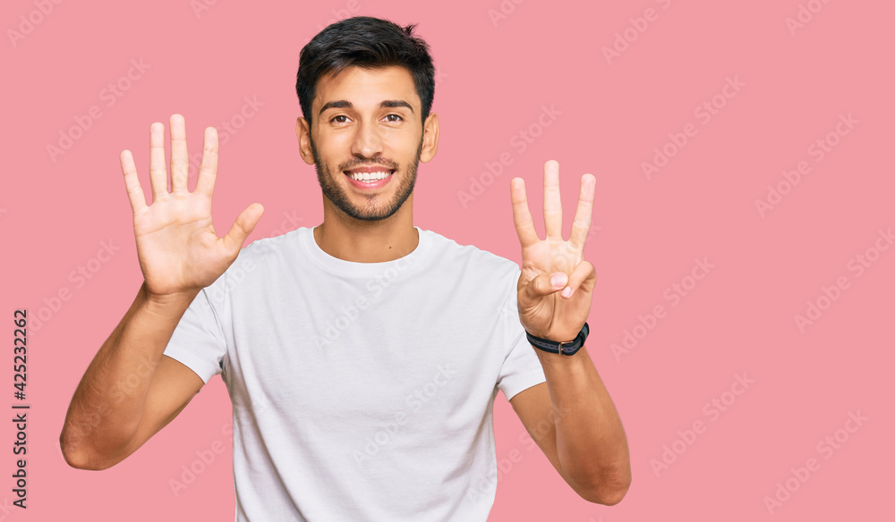 Young handsome man wearing casual white tshirt showing and pointing up with fingers number eight while smiling confident and happy. Young handsome man wearing casual white tshirt showing and pointing up with fingers number eight while smiling confident and happy.