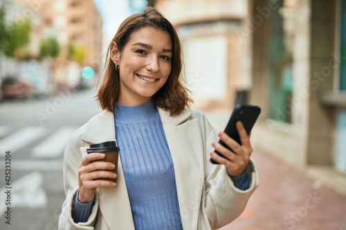 Young hispanic woman using smartphone and drinking coffee at the city.