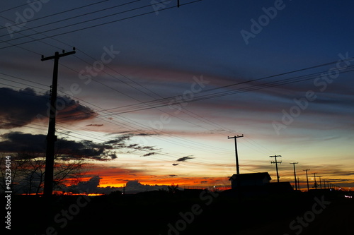 Colorful tropical sunset, power poles strung together with wires along a straight long road. Rorainópolis, state of Roraima, Brazil. photo