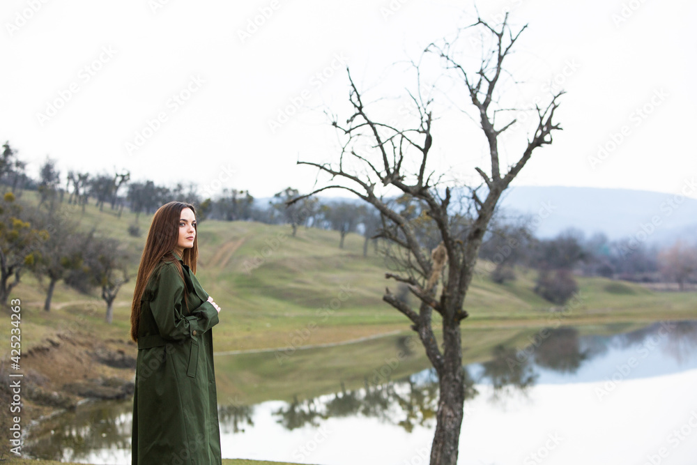 Image of young beautiful woman wearing rain jacket in cold weather. Thinker european girl in spring nature.