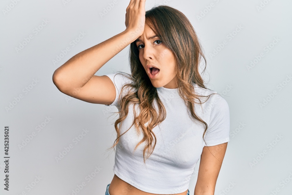Young brunette woman wearing casual white t shirt surprised with hand on head for mistake, remember error. forgot, bad memory concept. Young brunette woman wearing casual white t shirt surprised with hand on head for mistake, remember error. forgot, bad memory concept.