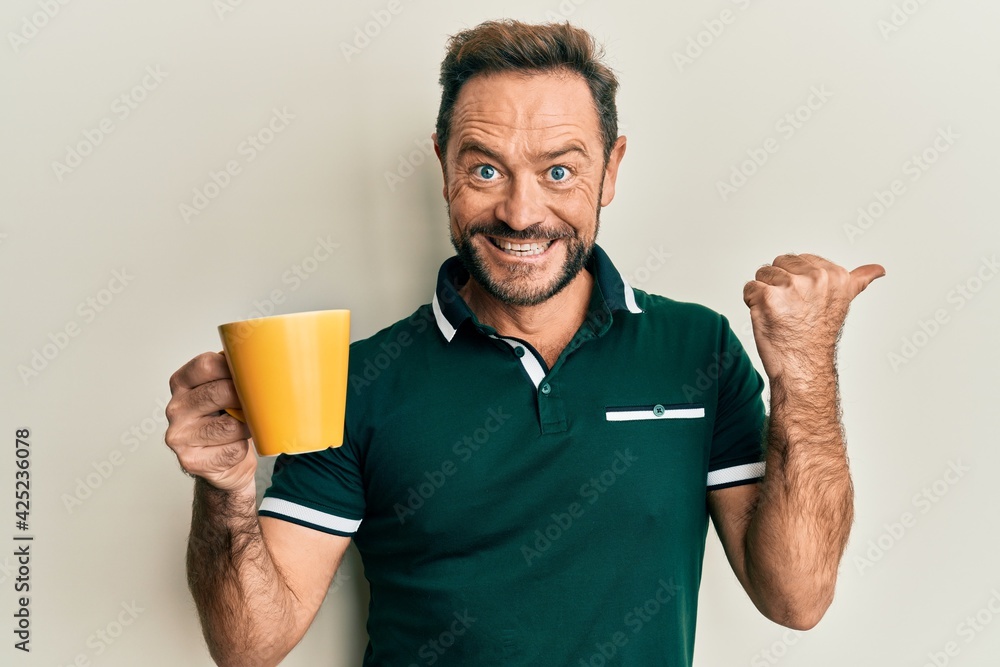 Middle age man drinking a cup of coffee pointing thumb up to the side smiling happy with open mouth Middle age man drinking a cup of coffee pointing thumb up to the side smiling happy with open mouth
