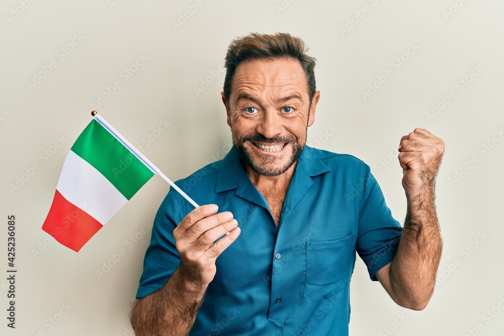 Middle age man holding italy flag screaming proud, celebrating victory and success very excited with raised arm Middle age man holding italy flag screaming proud, celebrating victory and success very excited with raised arm