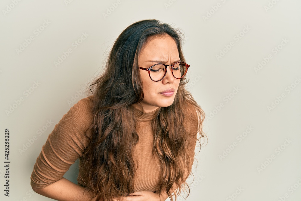 Young hispanic girl wearing casual clothes and glasses with hand on stomach because indigestion, painful illness feeling unwell. ache concept. Young hispanic girl wearing casual clothes and glasses with hand on stomach because indigestion, painful illness feeling unwell. ache concept.