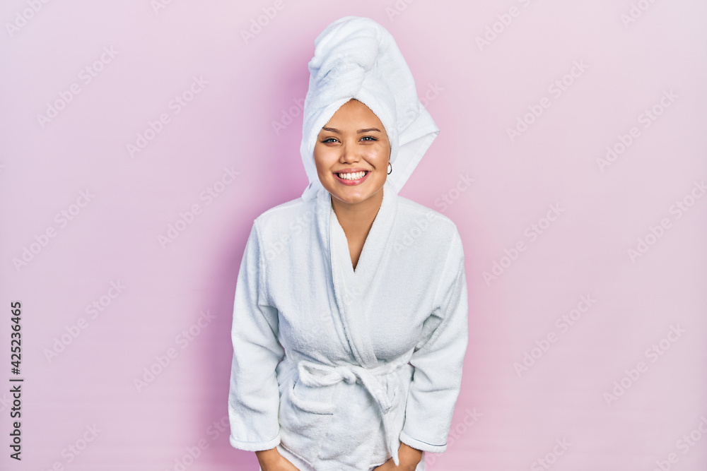 Young hispanic girl wearing shower towel cap and bathrobe looking positive and happy standing and smiling with a confident smile showing teeth Young hispanic girl wearing shower towel cap and bathrobe looking positive and happy standing and smiling with a confident smile showing teeth