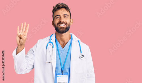 Young hispanic man wearing doctor uniform and stethoscope showing and pointing up with fingers number four while smiling confident and happy. © Krakenimages.com