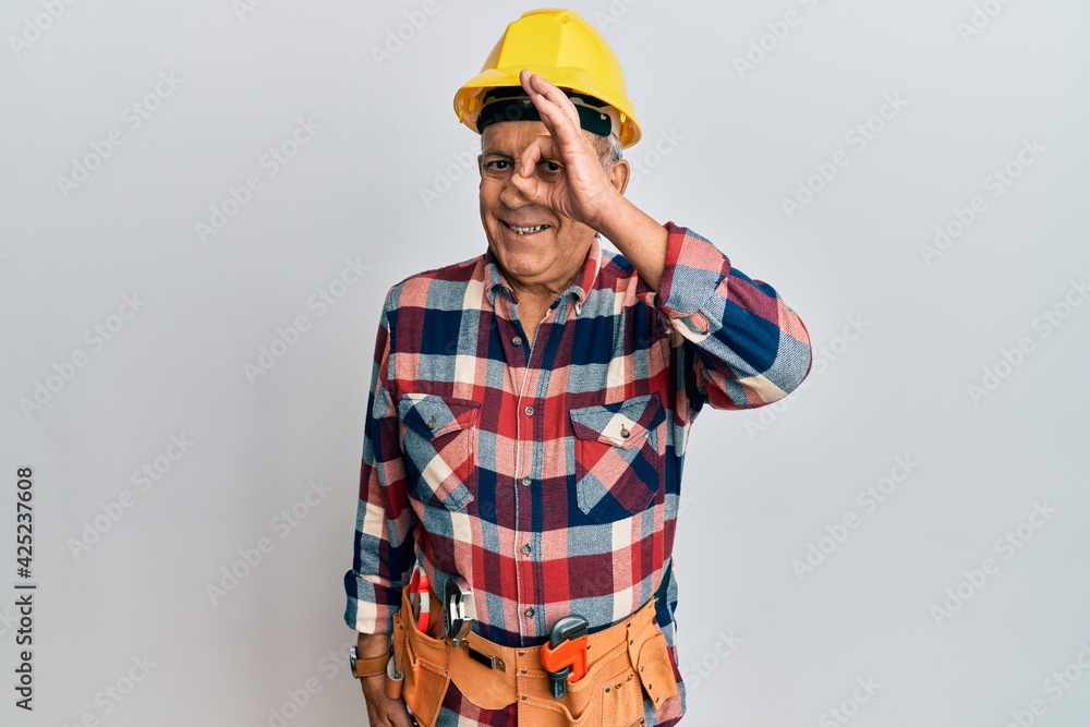 Senior hispanic man wearing handyman uniform doing ok gesture with hand smiling, eye looking through fingers with happy face. Senior hispanic man wearing handyman uniform doing ok gesture with hand smiling, eye looking through fingers with happy face.