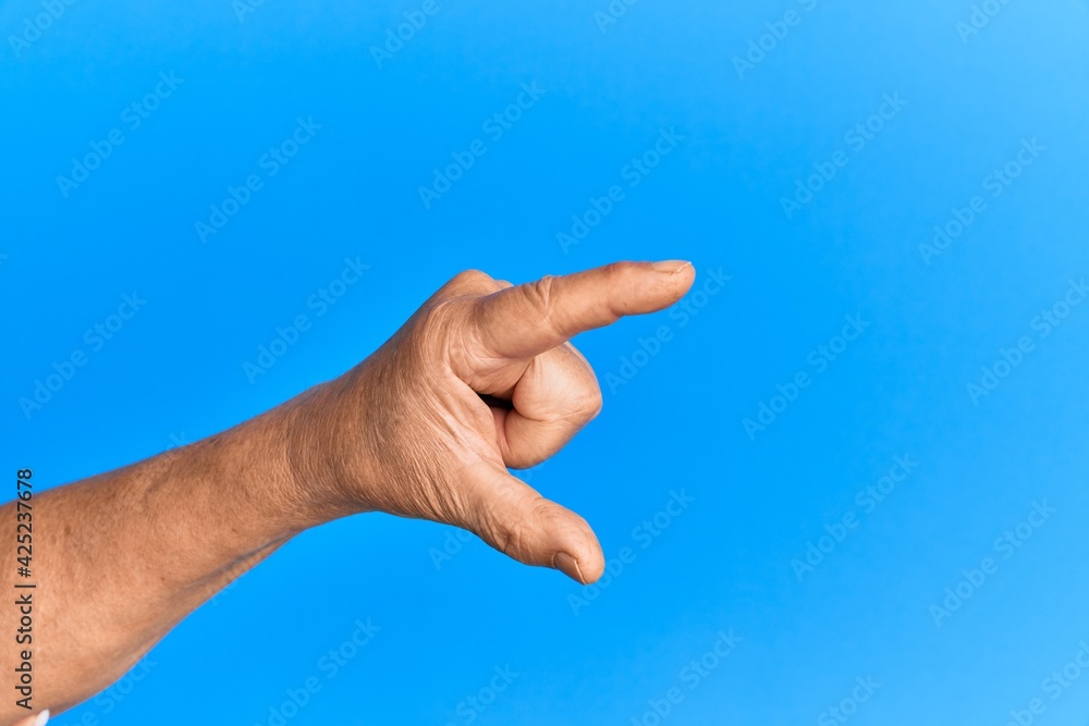 Hand of senior hispanic man over blue isolated background picking and taking invisible thing, holding object with fingers showing space Hand of senior hispanic man over blue isolated background picking and taking invisible thing, holding object with fingers showing space