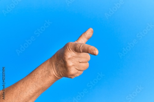 Hand of senior hispanic man over blue isolated background pointing forefinger to the camera, choosing and indicating towards direction