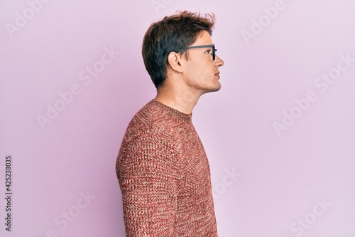 Handsome caucasian man wearing casual sweater and glasses looking to side, relax profile pose with natural face with confident smile.