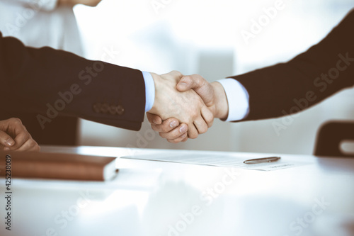 Business people shaking hands at meeting or negotiation, close-up. Group of unknown businessmen, and a woman on the background in a modern office. Teamwork, partnership and handshake concept