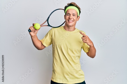 Handsome caucasian man playing tennis holding racket and ball smiling happy pointing with hand and finger © Krakenimages.com