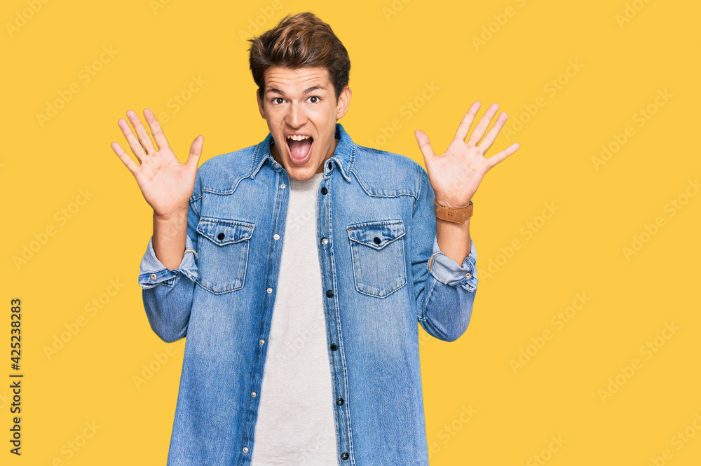 Handsome caucasian man wearing casual denim jacket celebrating crazy and amazed for success with arms raised and open eyes screaming excited. winner concept Handsome caucasian man wearing casual denim jacket celebrating crazy and amazed for success with arms raised and open eyes screaming excited. winner concept
