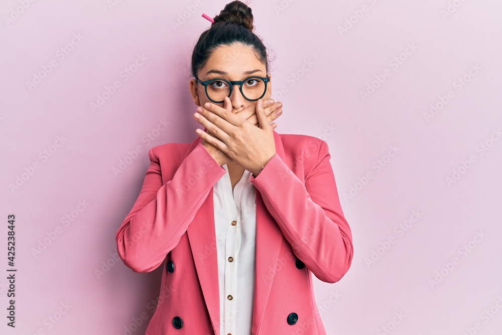 Beautiful middle eastern woman wearing business jacket and glasses shocked covering mouth with hands for mistake. secret concept. Beautiful middle eastern woman wearing business jacket and glasses shocked covering mouth with hands for mistake. secret concept.