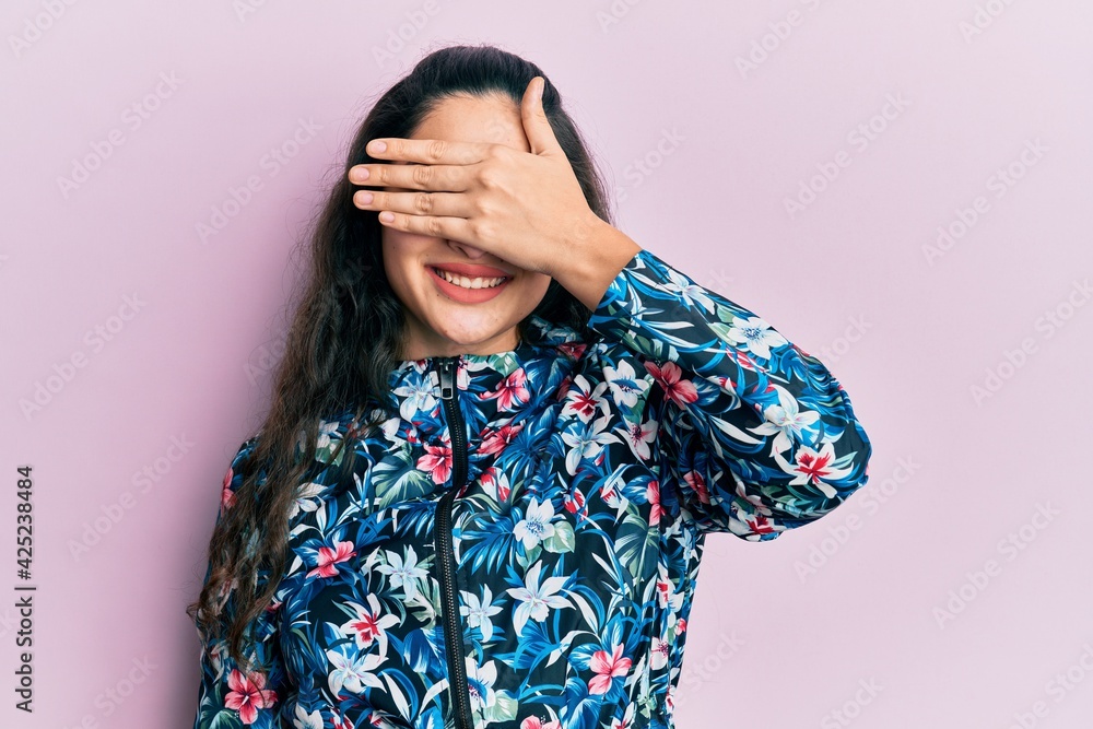 Beautiful middle eastern woman wearing casual floral jacket smiling and laughing with hand on face covering eyes for surprise. blind concept. Beautiful middle eastern woman wearing casual floral jacket smiling and laughing with hand on face covering eyes for surprise. blind concept.
