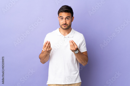 Young handsome man isolated on purple background making money gesture but is ruined