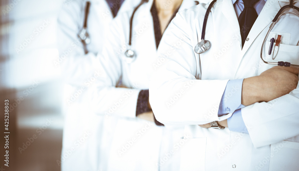 Group of modern doctors standing as a team with crossed arms and stethoscopes in hospital office. Physicians ready to examine and help patients. Medical help, insurance in health care, best desease Group of modern doctors standing as a team with crossed arms and stethoscopes in hospital office. Physicians ready to examine and help patients. Medical help, insurance in health care, best desease