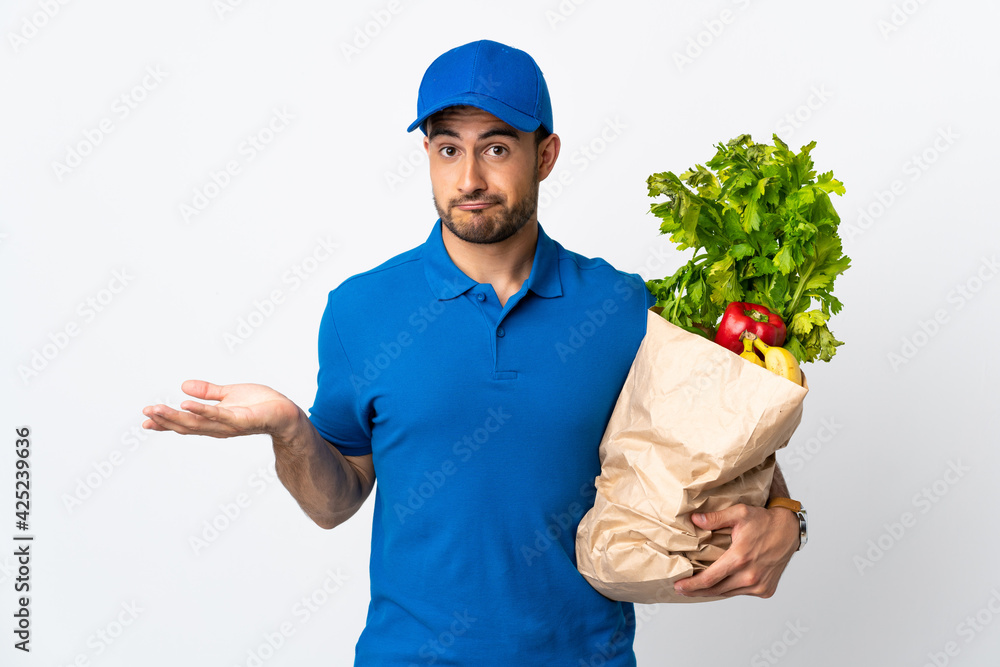 Delivery man with vegetables isolated on white background making doubts gesture while lifting the shoulders Delivery man with vegetables isolated on white background making doubts gesture while lifting the shoulders