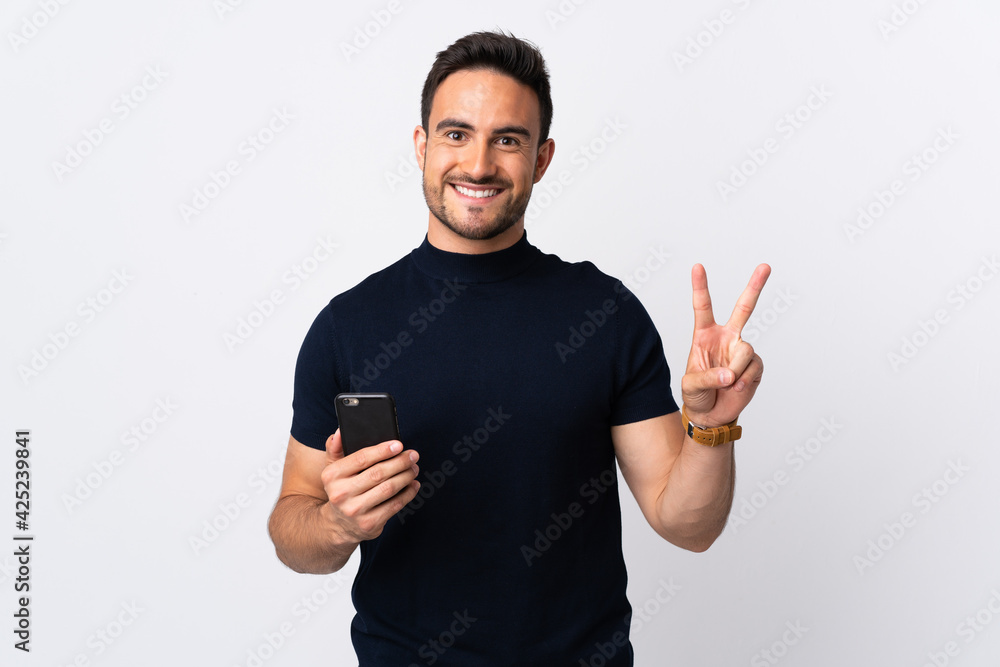 Young caucasian man using mobile phone isolated on white background smiling and showing victory sign Young caucasian man using mobile phone isolated on white background smiling and showing victory sign