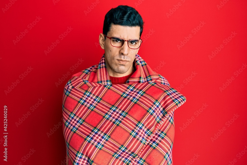 Handsome hispanic man wrapped in a red warm red blanket skeptic and nervous, frowning upset because of problem. negative person. Handsome hispanic man wrapped in a red warm red blanket skeptic and nervous, frowning upset because of problem. negative person.