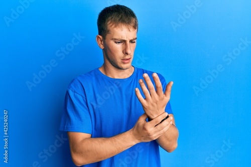 Young caucasian man wearing casual blue t shirt suffering pain on hands and fingers, arthritis inflammation