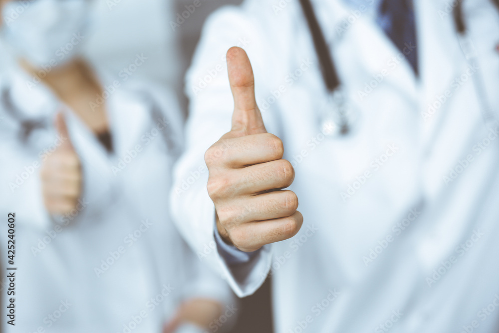 Unknown man-doctor and woman standing straight as a team and showing Ok sign with thumbs up in modern clinic. Medicine concept during Coronavirus pandemic. Covid 2019 Unknown man-doctor and woman standing straight as a team and showing Ok sign with thumbs up in modern clinic. Medicine concept during Coronavirus pandemic. Covid 2019