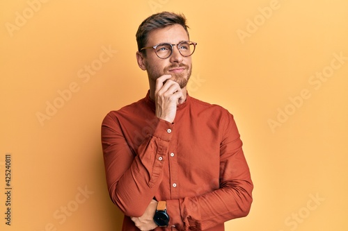 Handsome caucasian man wearing casual clothes and glasses thinking concentrated about doubt with finger on chin and looking up wondering