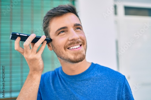 Young caucasian man smiling happy listening audio message using smartphone at the city.