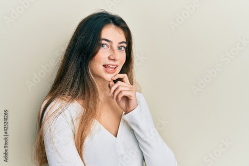 Young caucasian woman wearing casual white t shirt smiling looking confident at the camera with crossed arms and hand on chin. thinking positive.