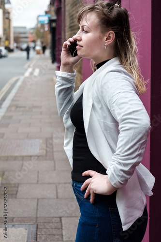 Young blonde woman standing beside a colourful wall with her phone.