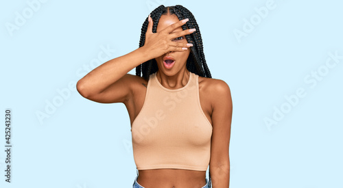 Beautiful hispanic woman wearing casual clothes peeking in shock covering face and eyes with hand, looking through fingers with embarrassed expression.