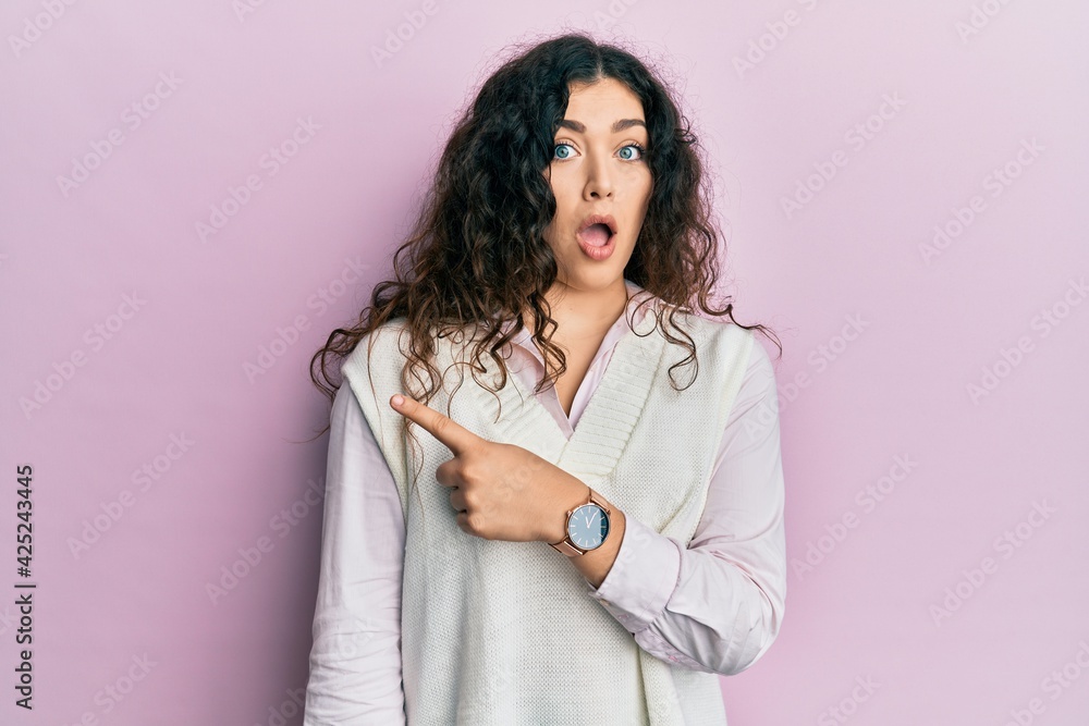 Young brunette woman with curly hair wearing casual clothes surprised pointing with finger to the side, open mouth amazed expression. Young brunette woman with curly hair wearing casual clothes surprised pointing with finger to the side, open mouth amazed expression.