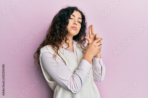 Young brunette woman with curly hair wearing casual clothes holding symbolic gun with hand gesture, playing killing shooting weapons, angry face © Krakenimages.com